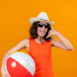 Kuva: Freepik <a href="https://www.freepik.com/free-photo/young-woman-with-short-hair-orange-shirt-wearing-sun-hat-sunglasses-holding-inflatable-ball-showing-call-me-gesture_10638141.htm#page=2&query=show%20me%20red&position=28&from_view=search&track=sph">Image by stockking</a> on Freepik